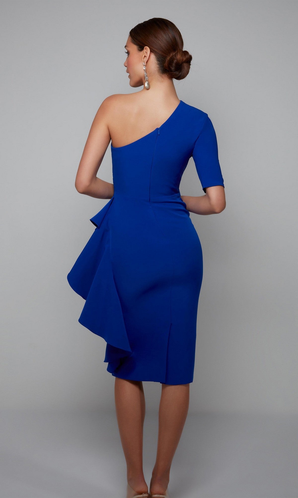 A woman faces away, wearing the royal blue Alyce 70006 Knee Length Semi-Formal Dress featuring one-shoulder ruffle detail and an asymmetrical sleeve.